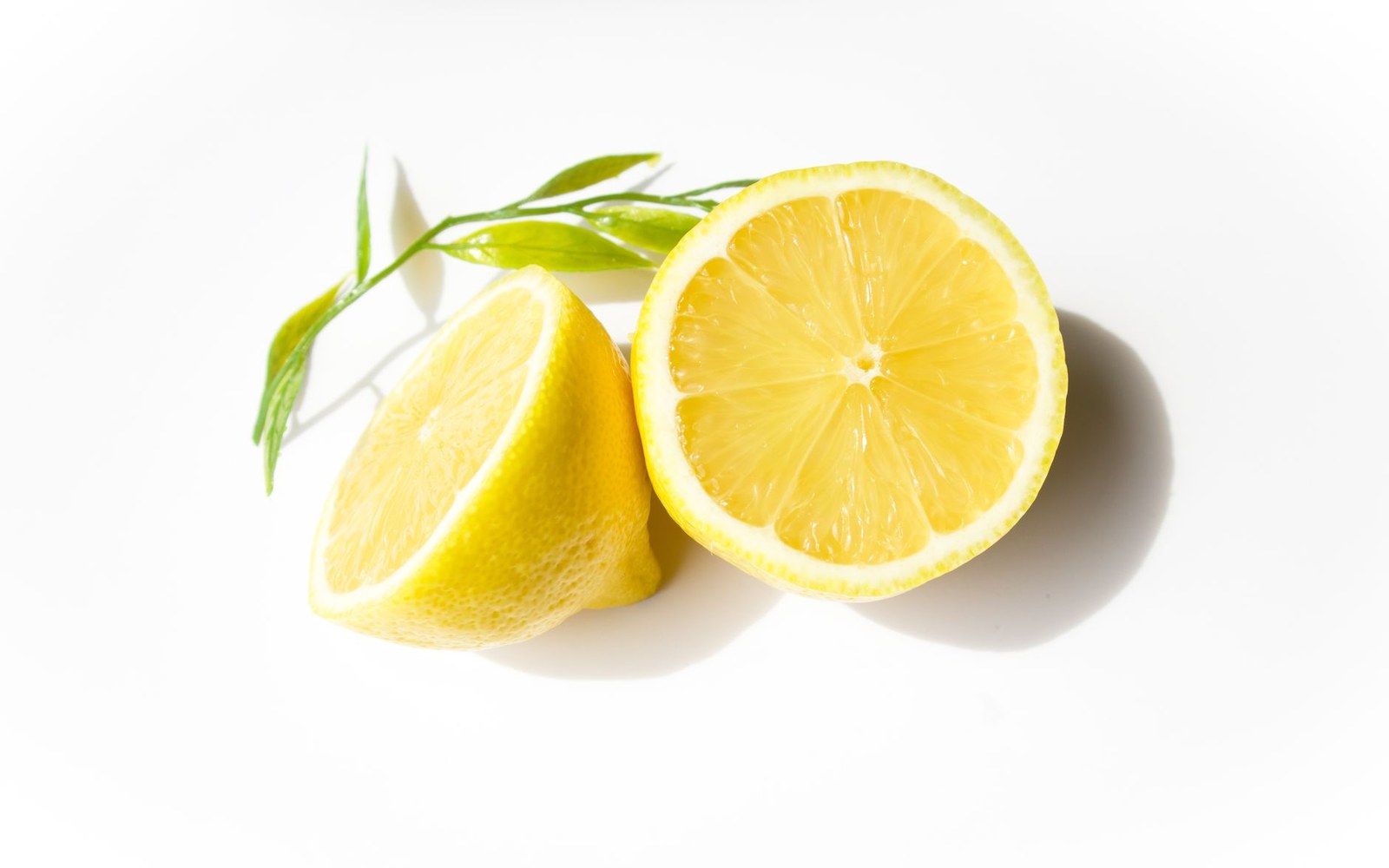 A lemon sliced in half beside green sprigs on a white background