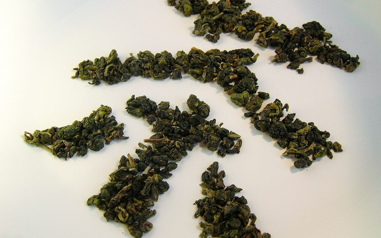 Rolled oolong tea leaves arranged in small clusters on a white surface