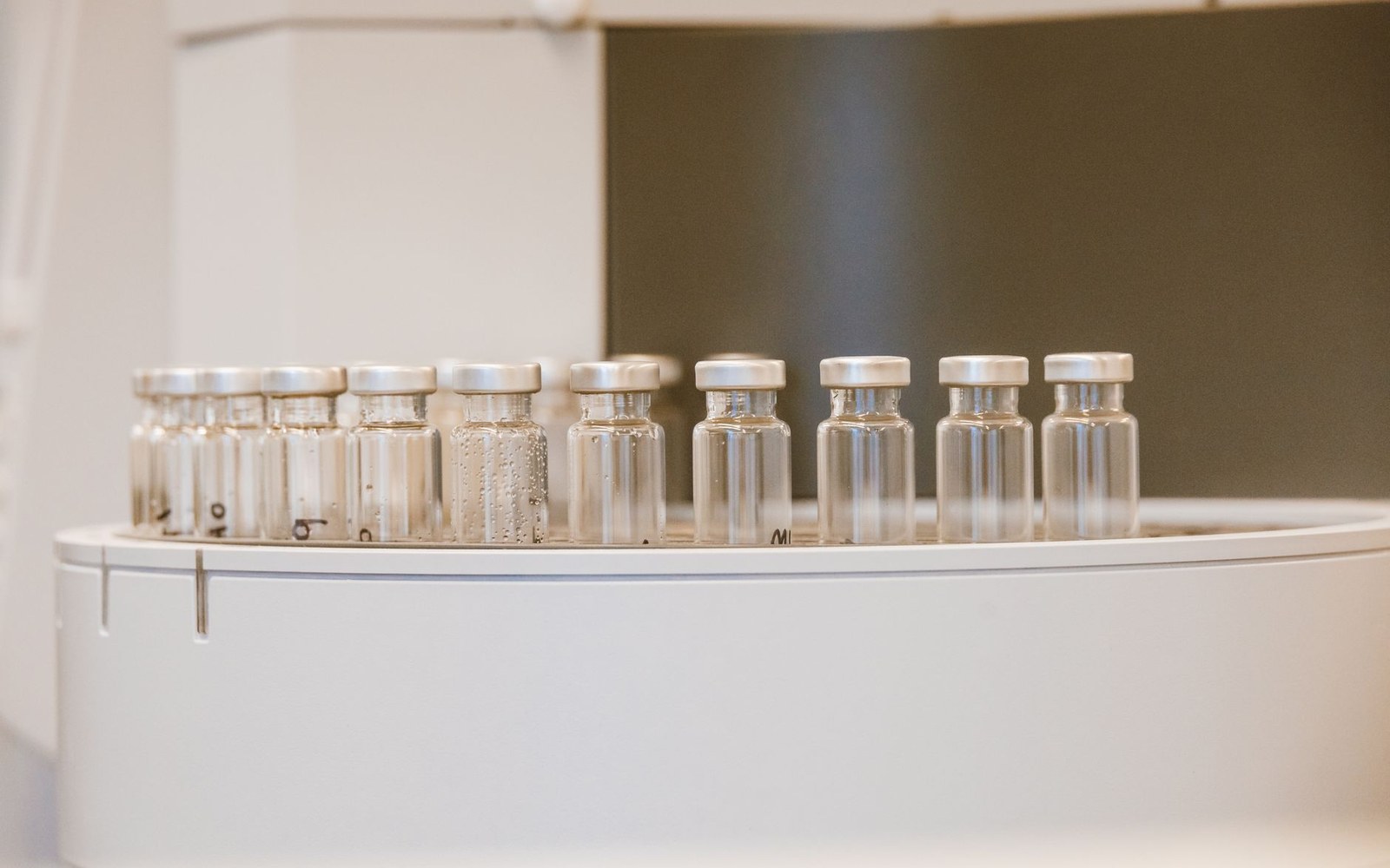A row of glass sample vials with metal caps lined up on lab equipment