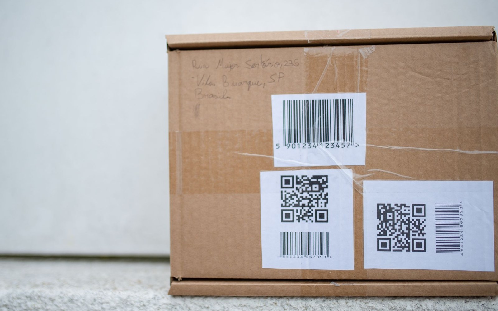 Cardboard shipping box with barcode and QR code labels and a handwritten address