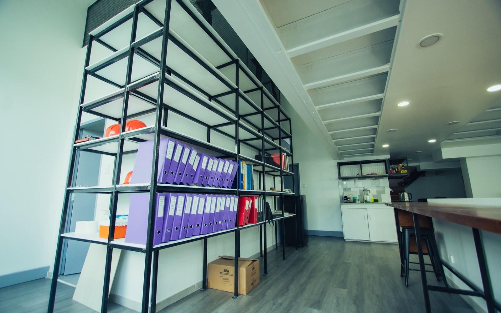 Metal shelving holds purple binders and files beside a kitchenette in an open office