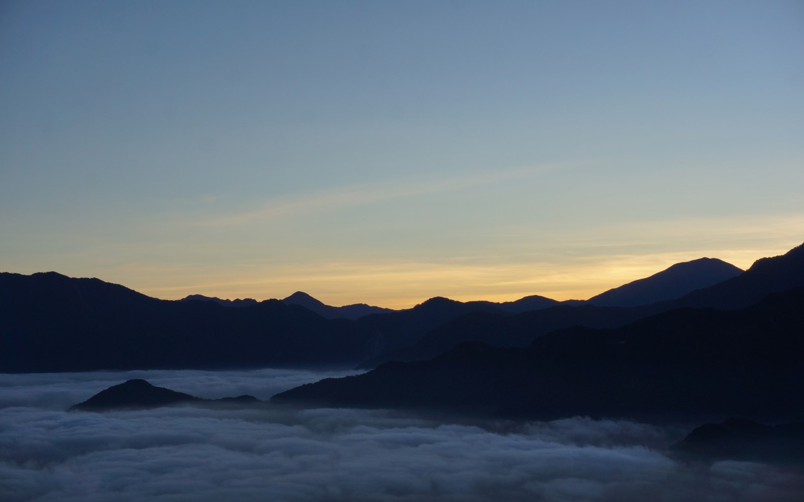 Cloud pouring over a forested ridge, backlit, long lens